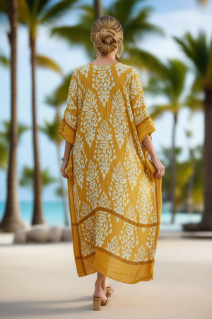 Woman in a yellow dress with white patterns walking on a beach with palm trees in the background
