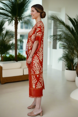 Woman wearing a red and white patterned dress standing in a modern indoor setting with plants.