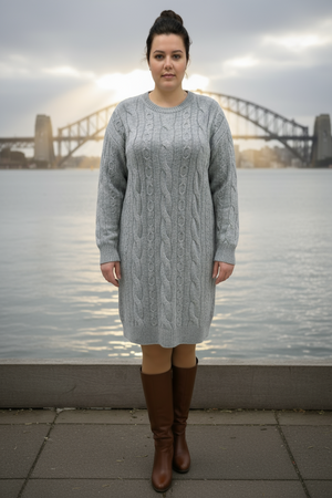 Woman wearing a gray cable knit dress with brown knee-high boots standing in front of a bridge over water.