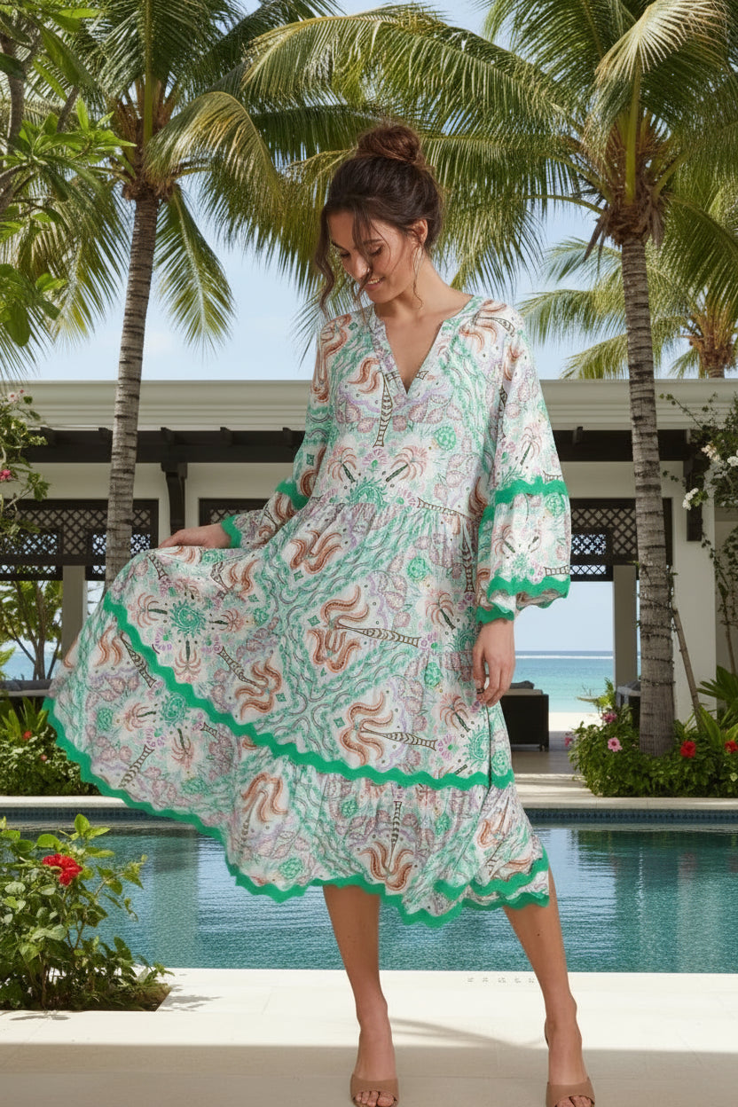 Woman wearing a patterned dress standing in a minimalistic room with a vase of flowers on a table.