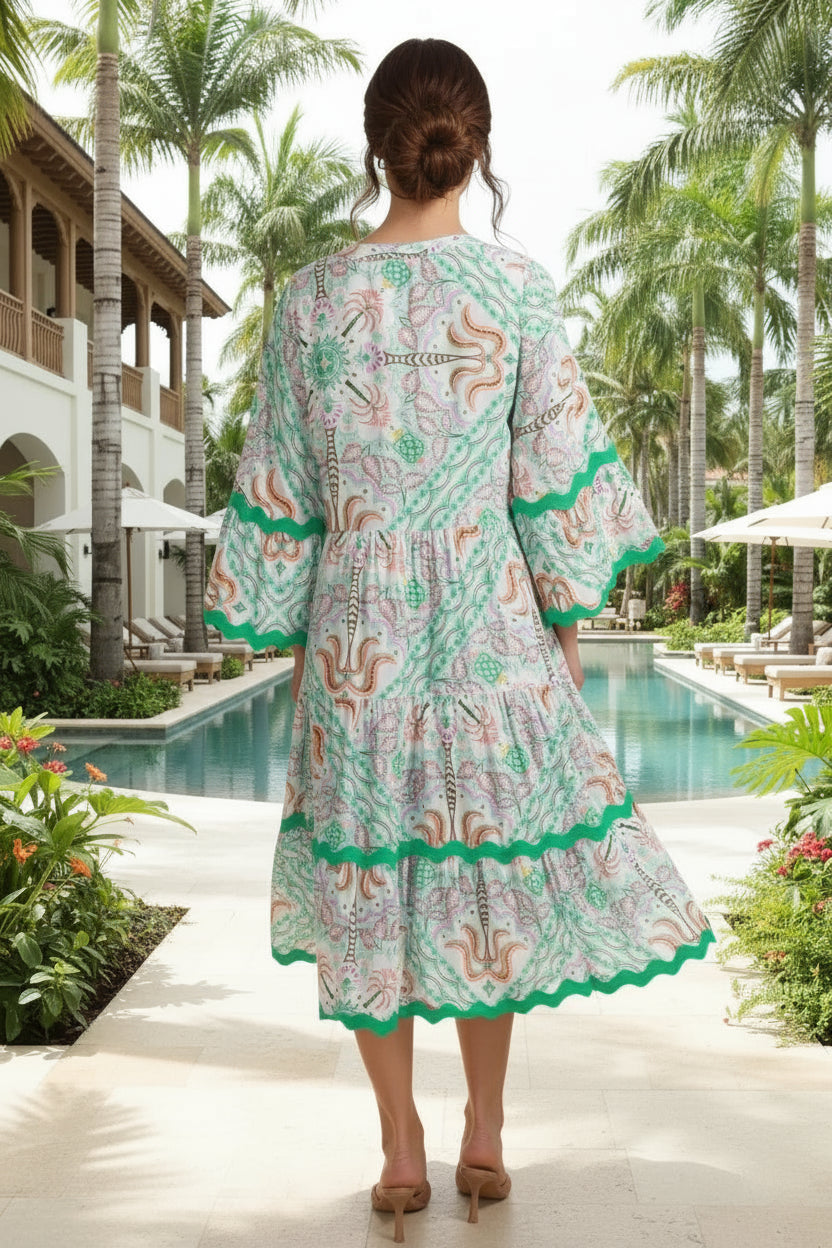 Woman wearing a patterned dress standing by a pool with palm trees in the background