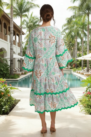 Woman wearing a patterned dress standing by a pool with palm trees in the background