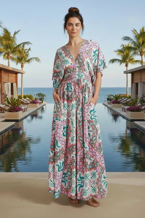 Woman wearing a colorful patterned dress standing outdoors with palm trees and a building in the background.