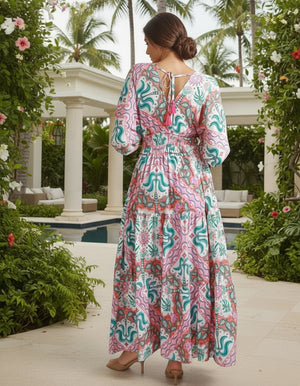 Woman in a colorful dress standing in a garden with palm trees and a pool.