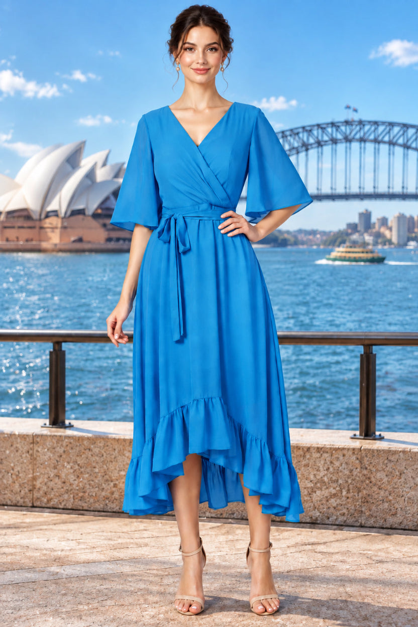 A woman wearing a bright blue surplice  midi dress with short flutter sleeves, a tie waist, and a ruffled high-low hem