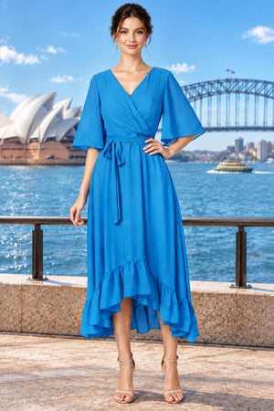 A woman wearing a bright blue surplice  midi dress with short flutter sleeves, a tie waist, and a ruffled high-low hem