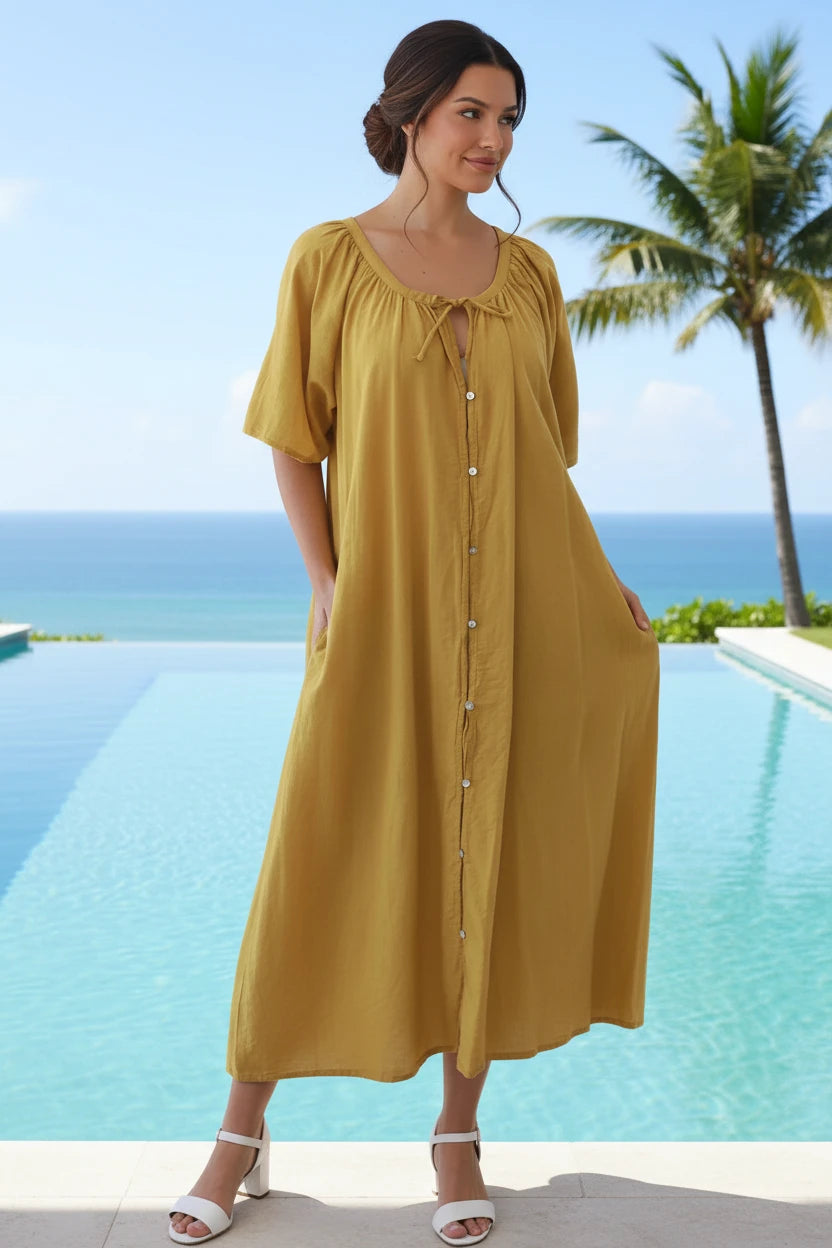Woman in a yellow dress standing by a pool with palm trees and ocean view