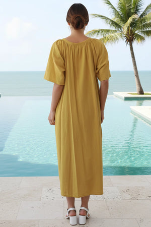 Woman in a yellow dress standing by a pool with palm trees in the background