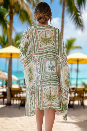 Woman wearing a patterned cover-up in a tropical setting with palm trees and beach umbrellas.