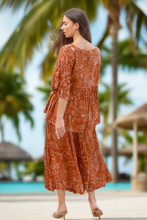 Woman in a rust-colored dress with a pattern standing by a poolside with palm trees in the background