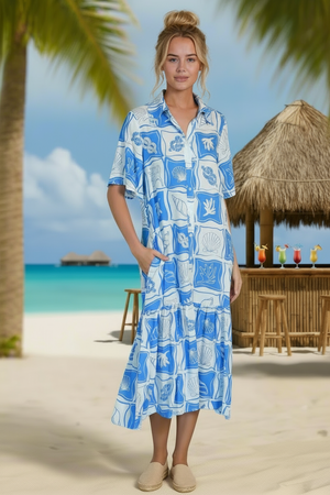 Woman in a blue and white patterned dress standing on a beach with palm trees and a thatched-roof hut in the background.