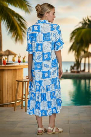 Woman wearing a blue and white patterned dress by a poolside with palm trees and a bar in the background.