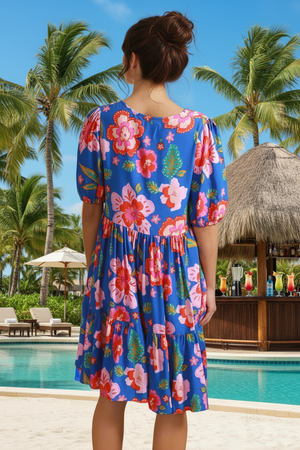 Woman wearing a colorful floral dress by a pool with palm trees in the background