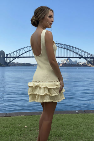 Woman in a yellow crochet dress standing by a waterfront with a bridge in the background