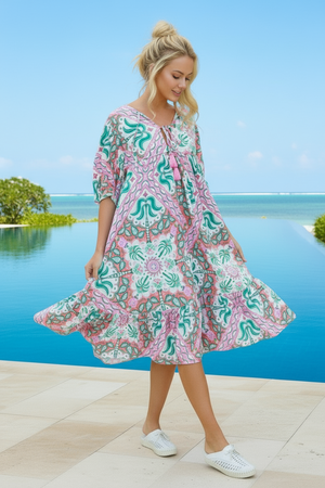 Woman wearing a colorful patterned dress by a poolside with palm trees in the background