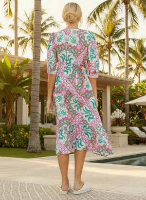 Woman in a colorful dress standing by a pool with palm trees in the background