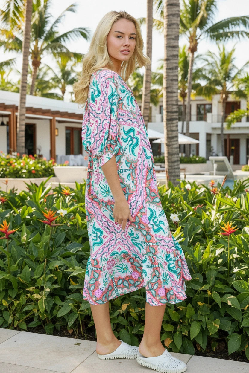 Woman wearing a colorful patterned dress by a poolside with palm trees in the background