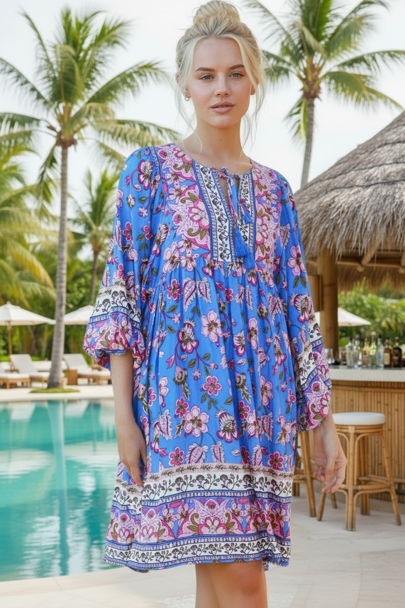 Woman in a blue floral dress standing by a pool with palm trees in the background