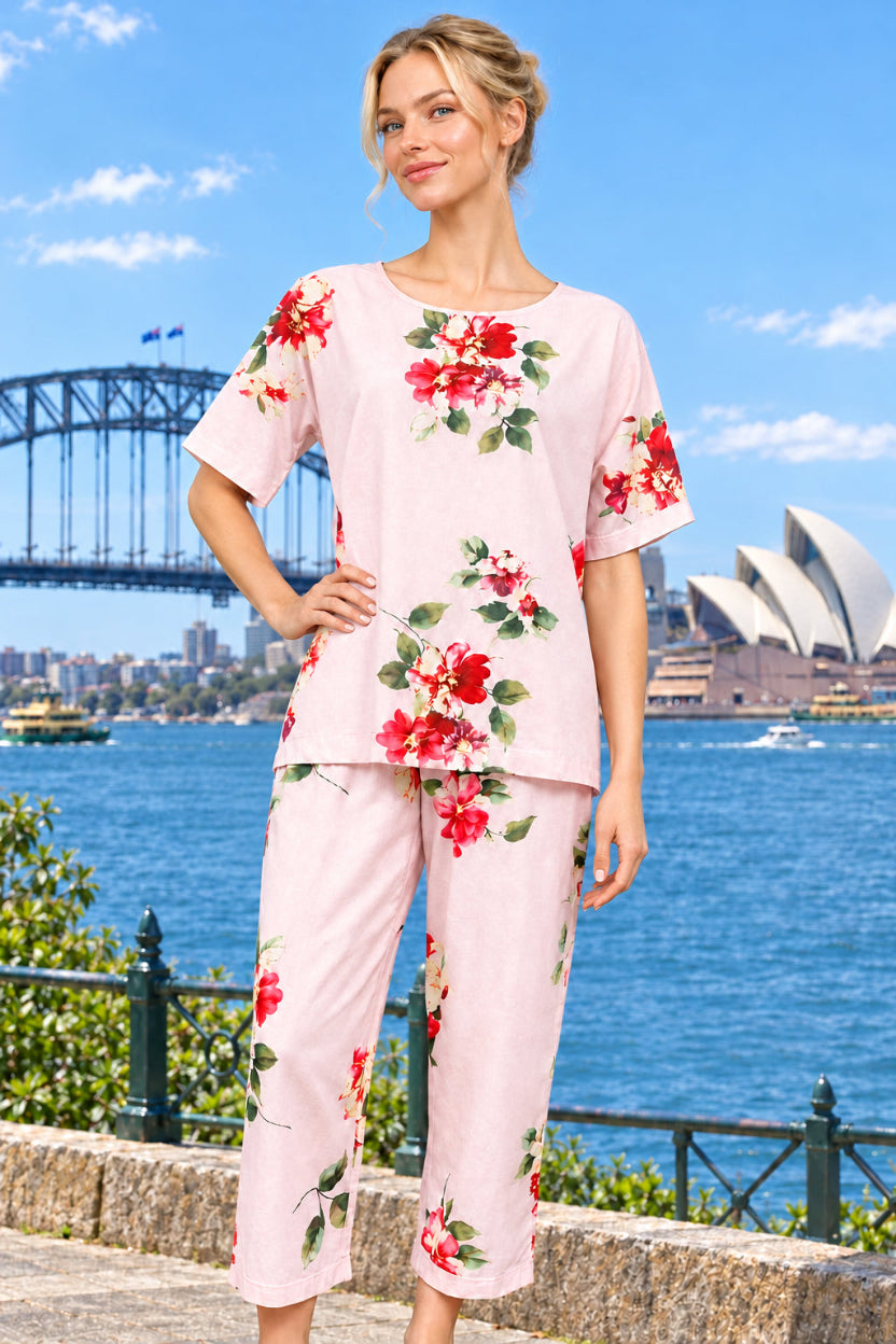 A woman wearing a cotton two-piece set, featuring a light pink short-sleeve top and matching capri pants with a red and green floral print. 