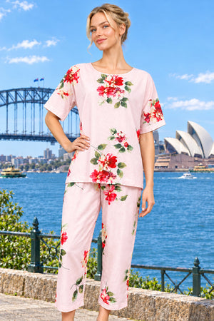 A woman wearing a cotton two-piece set, featuring a light pink short-sleeve top and matching capri pants with a red and green floral print. 