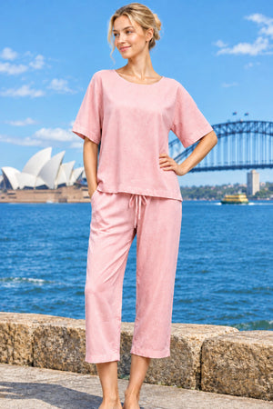 A woman wearing a cotton two-piece baby pink lounge set consisting of a short-sleeve top and matching capri pants