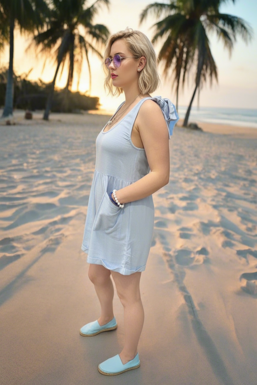 Woman in a light blue dress standing on a sandy path with palm trees in the background