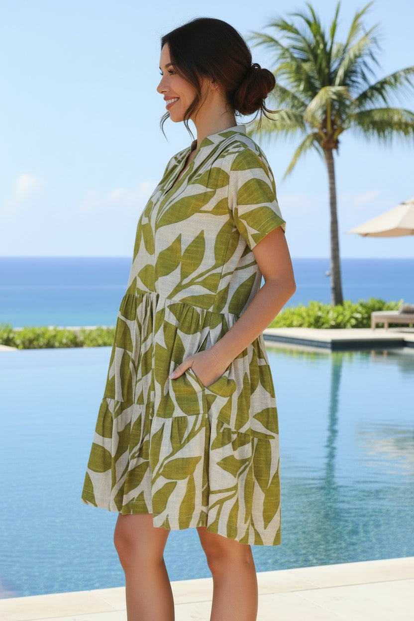 Woman wearing a green and white leaf-patterned dress standing against a stone wall.