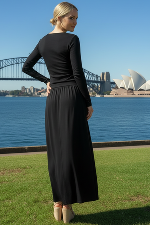 Woman in a long sleeve black maxi dress standing in front of the Sydney Harbour Bridge and Opera House.