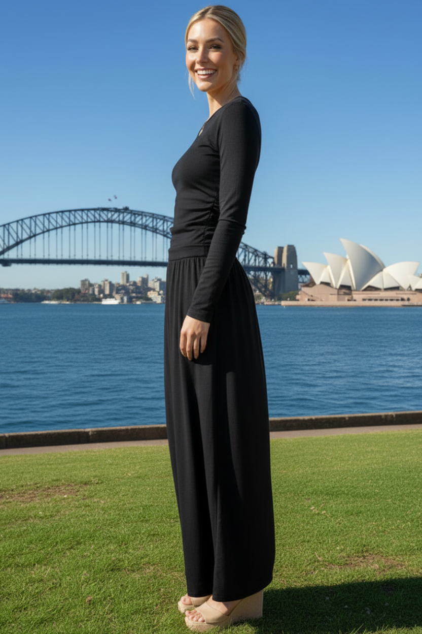 Woman in a long sleeve black maxi dress standing in front of the Sydney Harbour Bridge and Opera House.