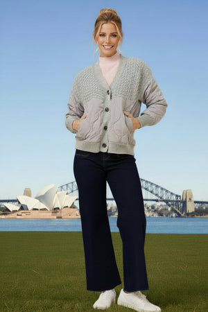 Woman wearing a light gray cardigan, pink shirt, dark blue jeans, and white sneakers.