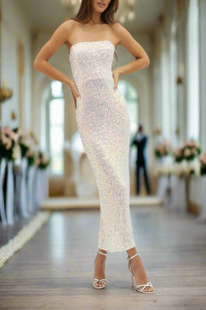A model wearing a strapless cowl back cocktail dress in pink sequins, with a boned corset bodice and spaghetti straps, standing in a grand room with a white decor.