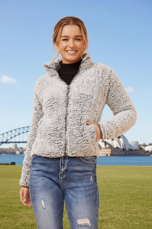 Woman wearing a gray fleece jacket with a blurred cityscape in the background