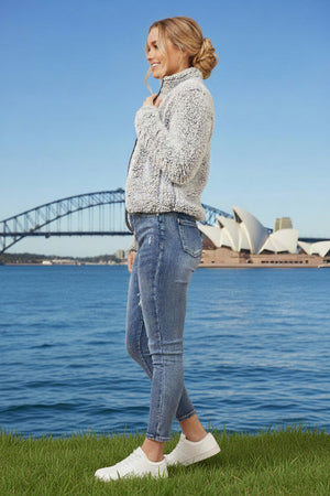 Woman standing on grass by water with a bridge and Opera House in the background