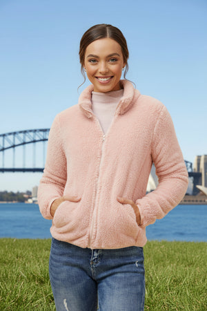 Woman wearing a pink jacket with a blurred cityscape and bridge in the background