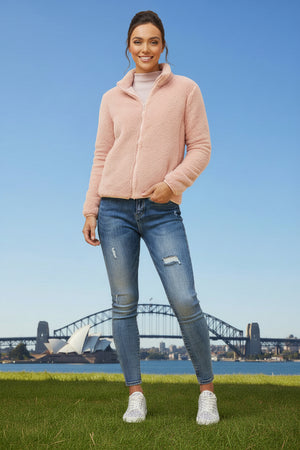Woman wearing a pink jacket and blue jeans standing in front of the Sydney Harbour Bridge.
