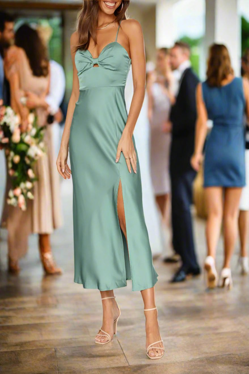 A woman wearing a green satin midi cocktail dress with a sweetheart neckline, front keyhole, and back zipper, standing at a social event.