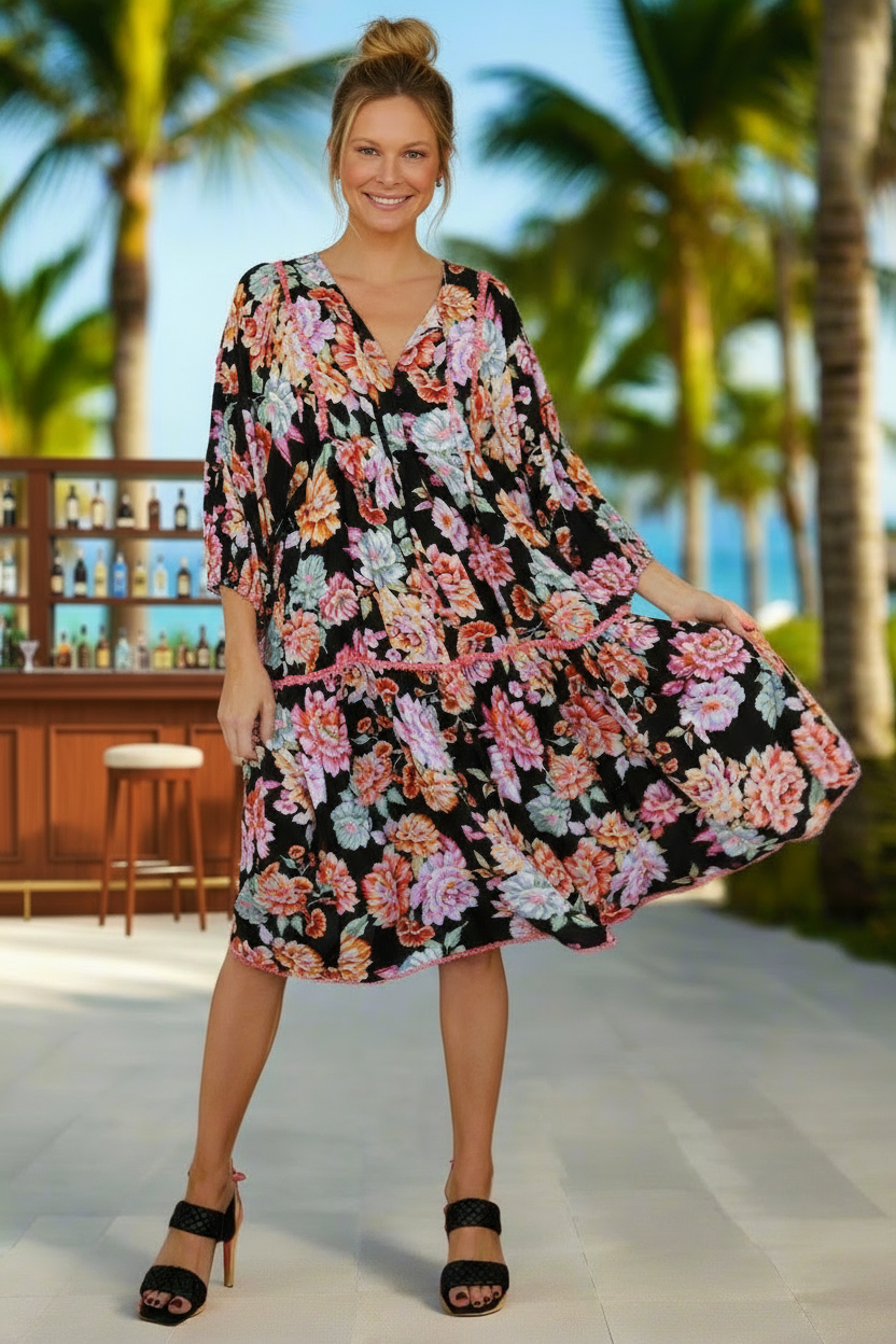 Woman in a floral dress standing on a tropical beach with palm trees and a bar in the background.