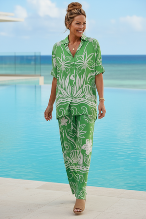 Woman in a green and white floral outfit standing on a beach with palm trees in the background.