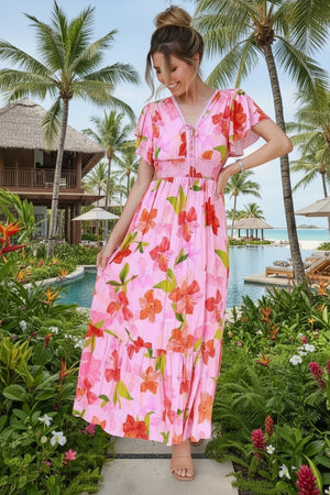Woman in a pink floral dress standing in a tropical setting with palm trees and a pool.