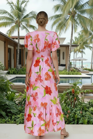 Woman in a pink floral dress standing in a tropical setting with palm trees and a pool.