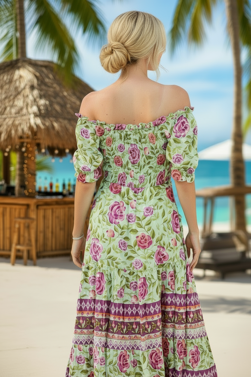 Woman in a floral dress standing on a tropical beach with palm trees and a bar in the background.