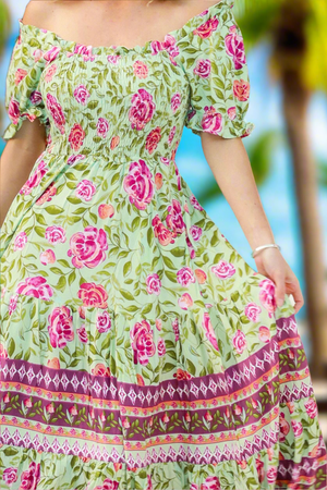 Green floral dress with pink flowers and colorful border against a blurred natural background