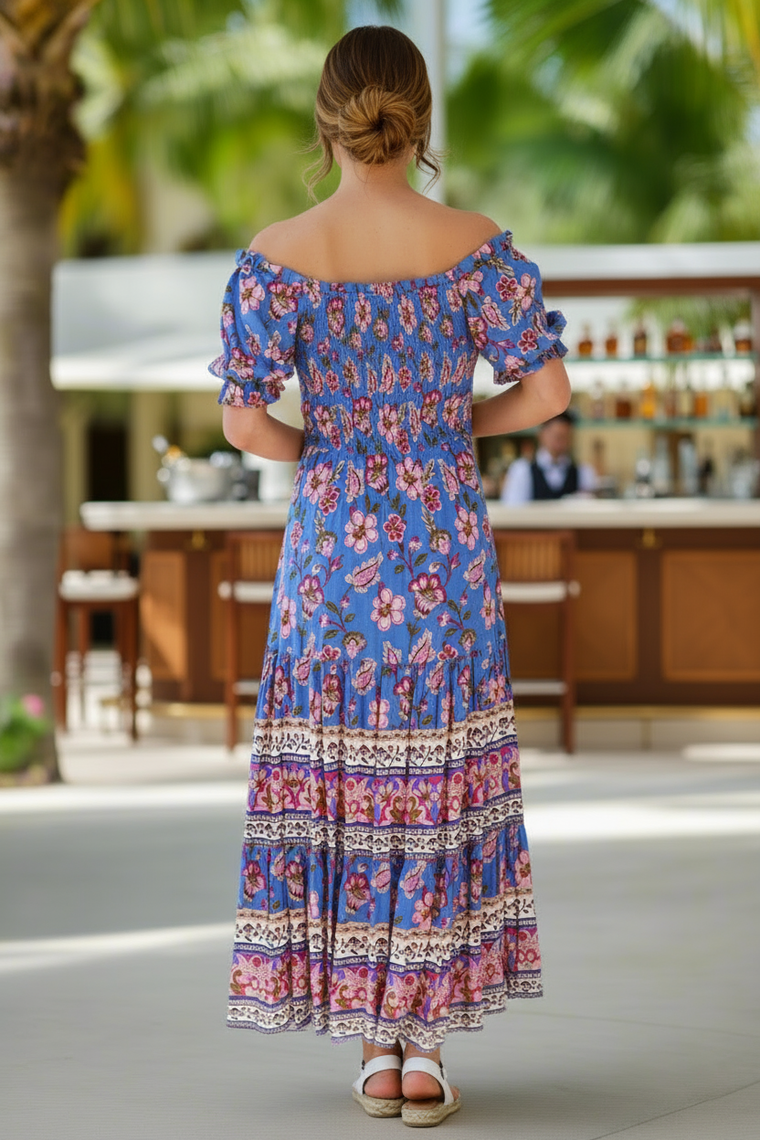 Woman wearing a blue floral dress in an outdoor setting with palm trees.