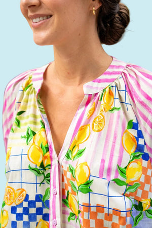 A close-up of a woman wearing a colourful dress with a lemon print, pink stripes, and checkered patterns 